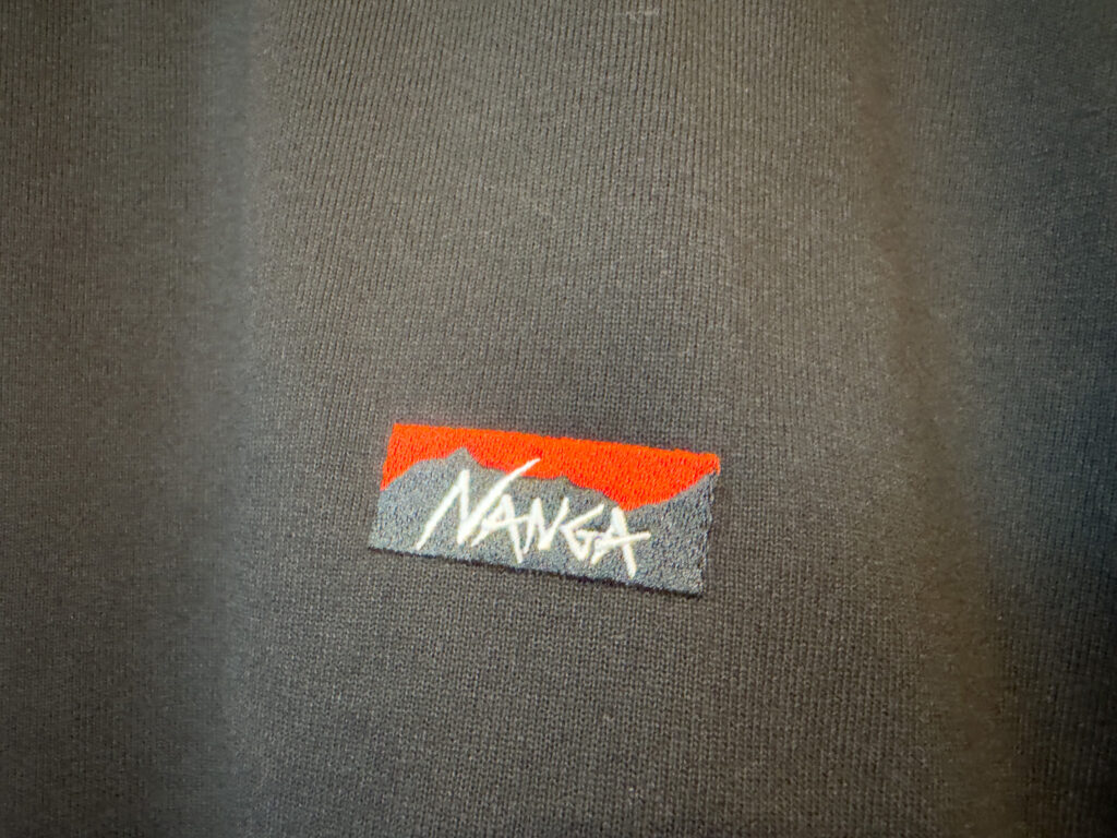ナンガ ECO HYBRID BOX LOGO EMBROIDERY TEEの左胸ボックスロゴ刺繍のアップ。赤とグレーの山のシルエットに白いNANGAの文字